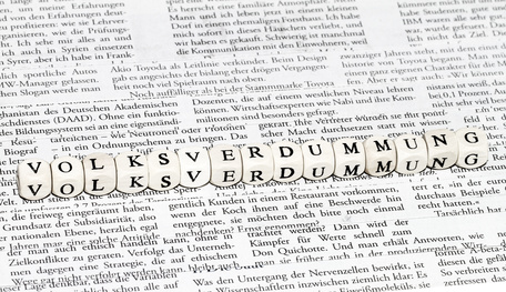 Das Wort "Volksverdummung" zusammengesetzt aus Buchstabenwürfeln vor gedrucktem Text