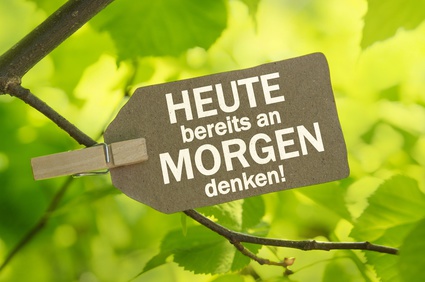 Schild mit Aufschrift "heute bereits an morgen denken!" vor Laubbaum