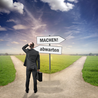 Ein Mann vor einer Weggabelung mit Wegweisern "machen!" und "abwarten!"